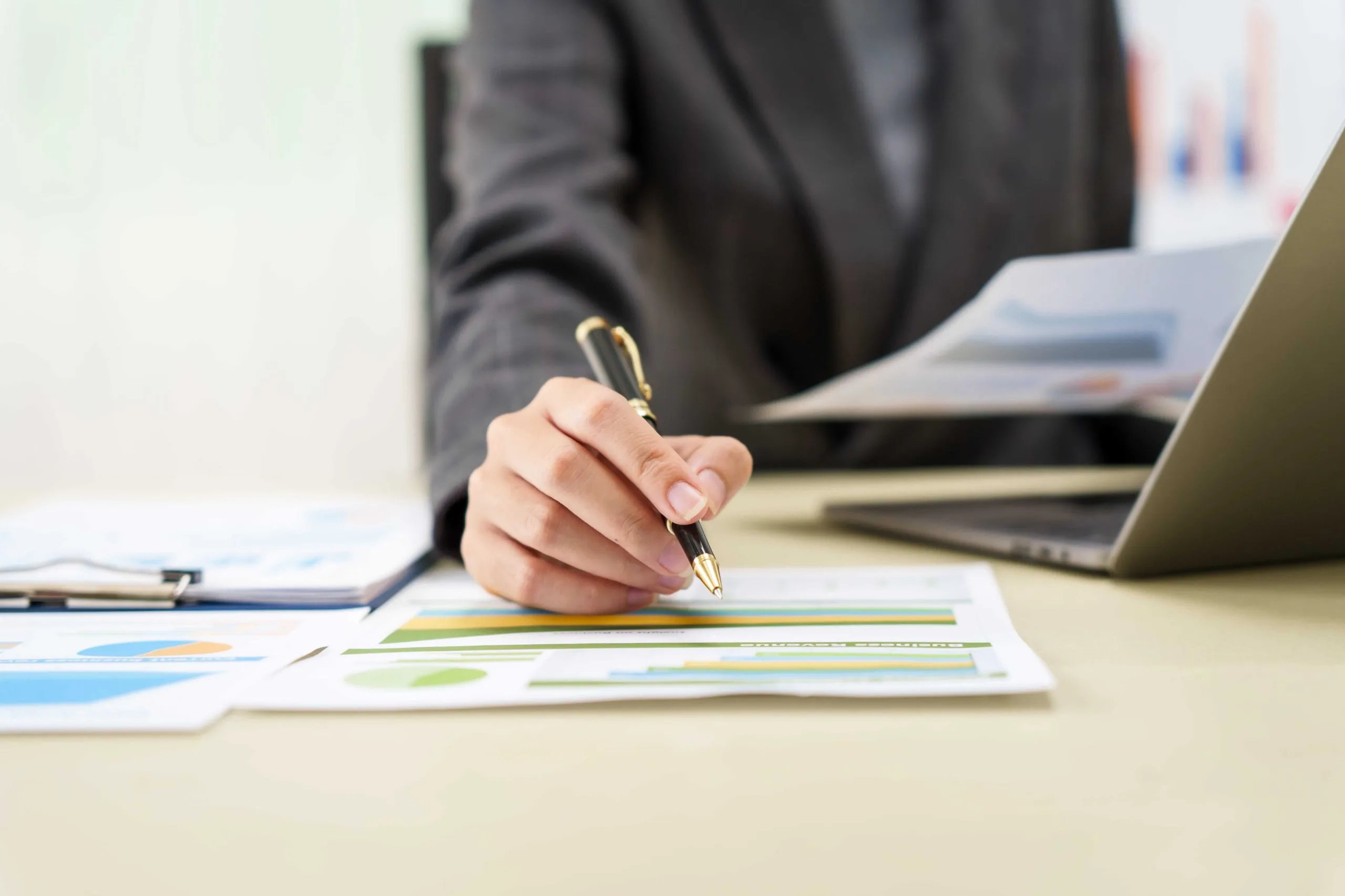 A person analyzes documents and graphs while working on a blog with a laptop and pen